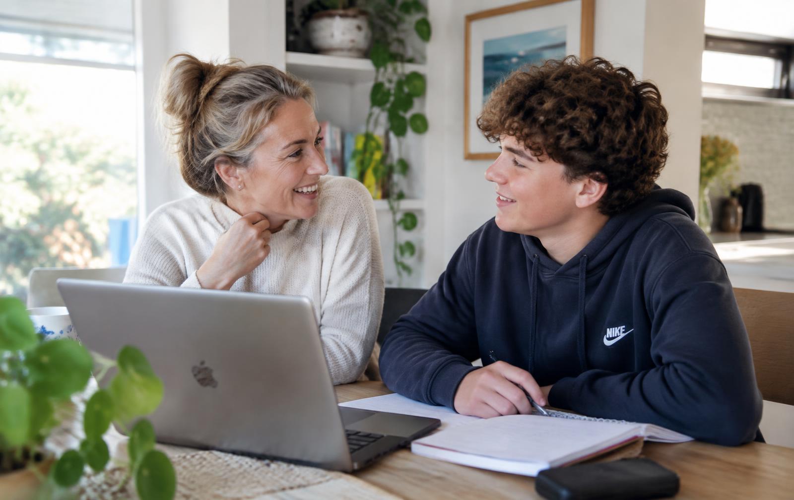A mother and her teenage son smiling at each other while planning next steps at the kitchen table